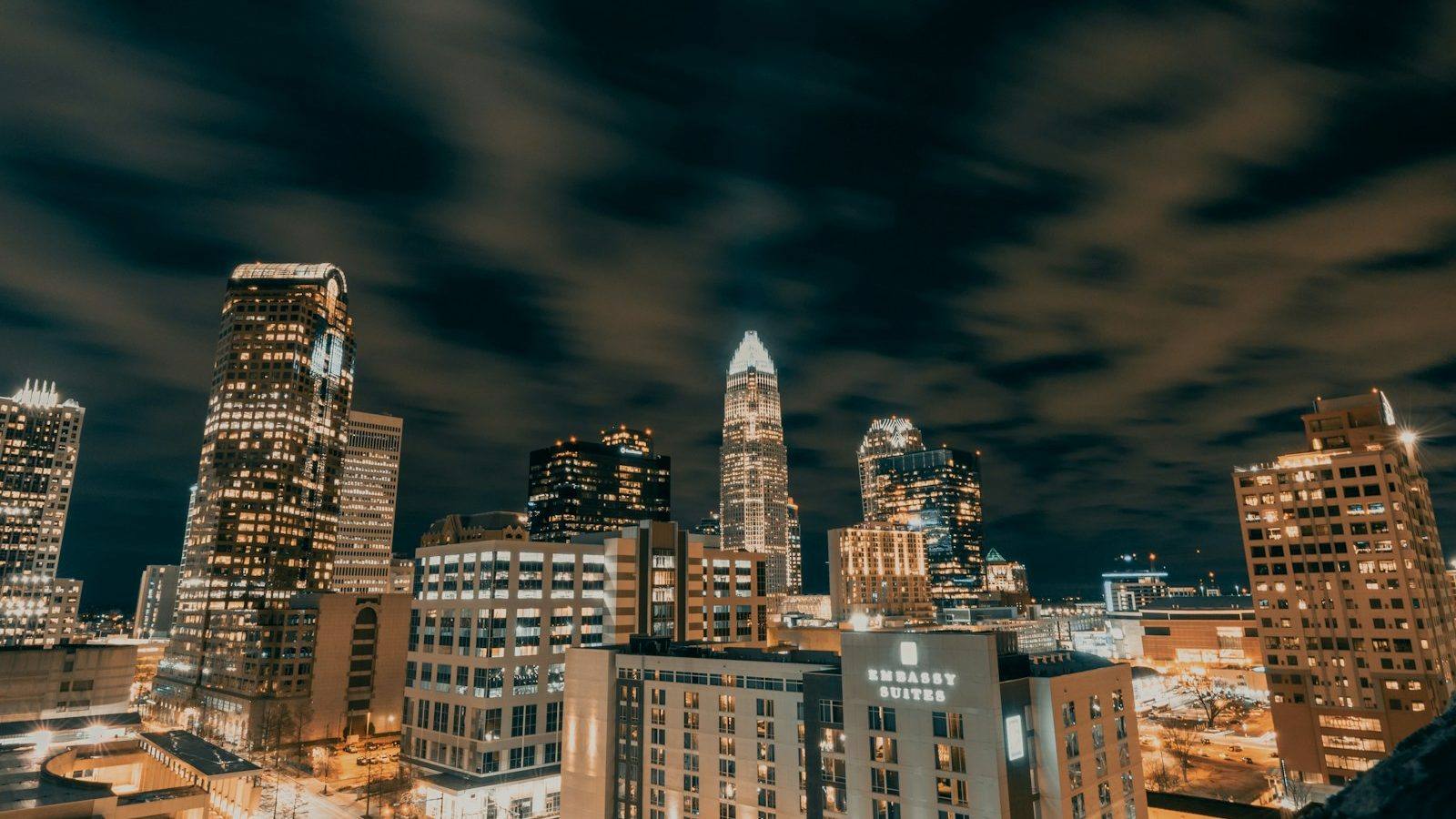 The lit towers of uptown Charlotte at night beneath a streaked, cloudy sky